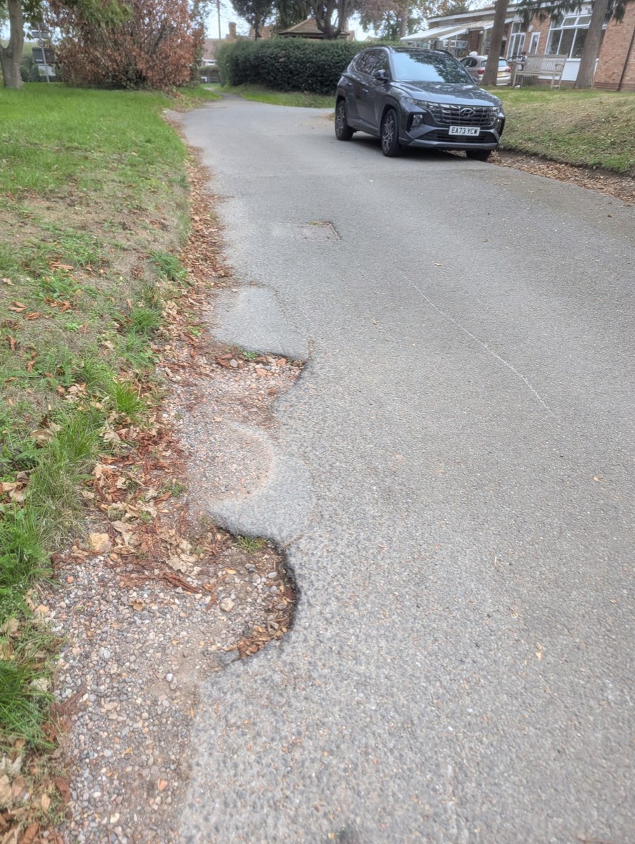Station Road past the village hall with no footway, a car in the carriageway