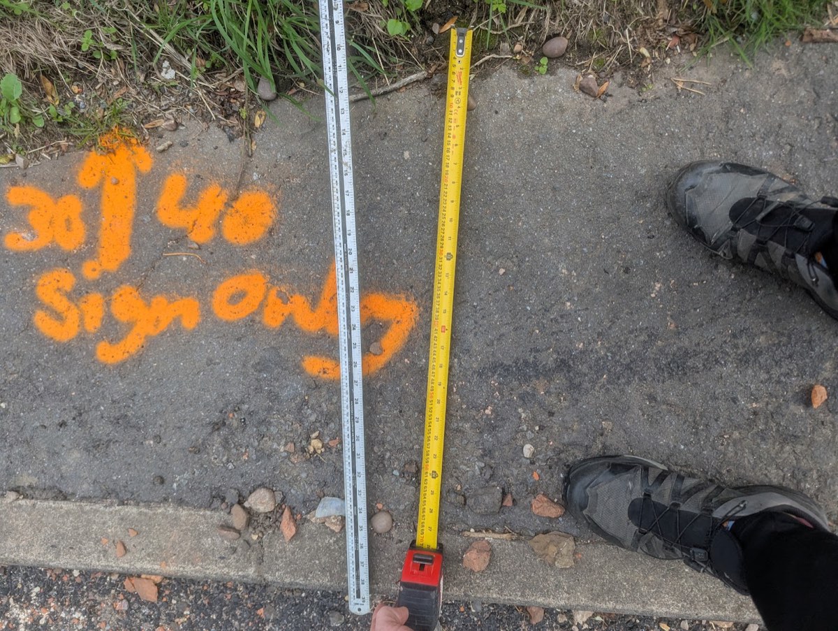 Two measuring rules laid across a narrow tarmac footway