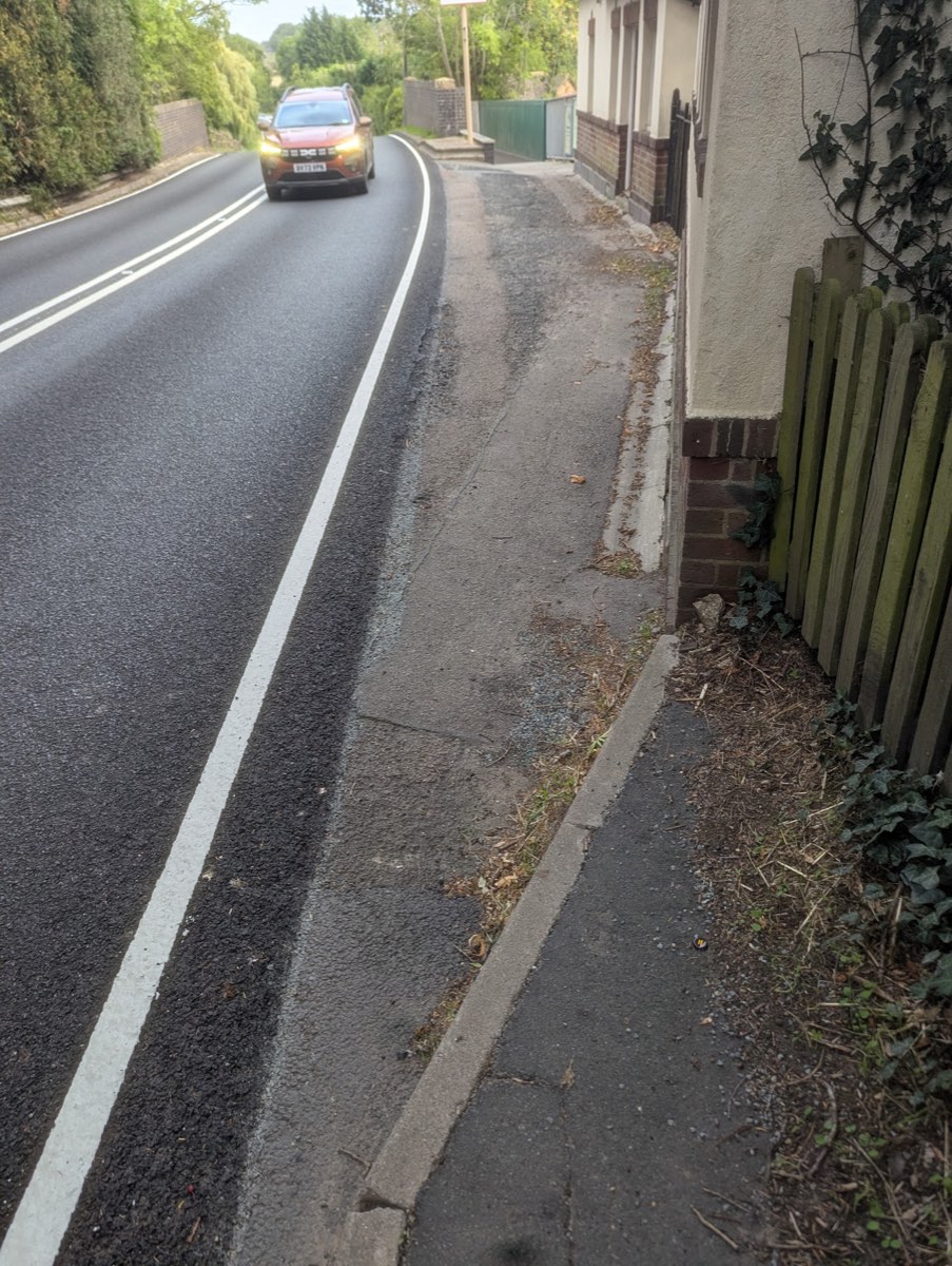 Station Road at the point the footway ends, fence on the left, car approaching